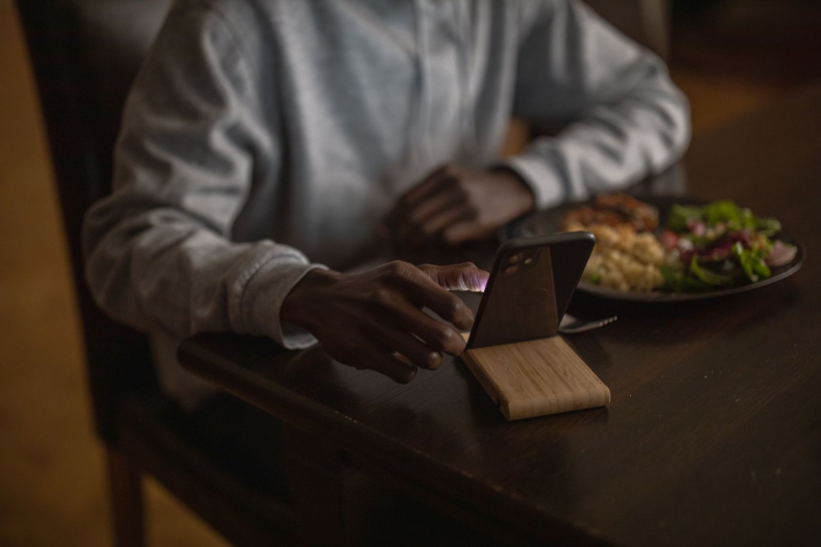 飲食店のテーブルで、料理の横に立てたスマートフォンを操作している手元
