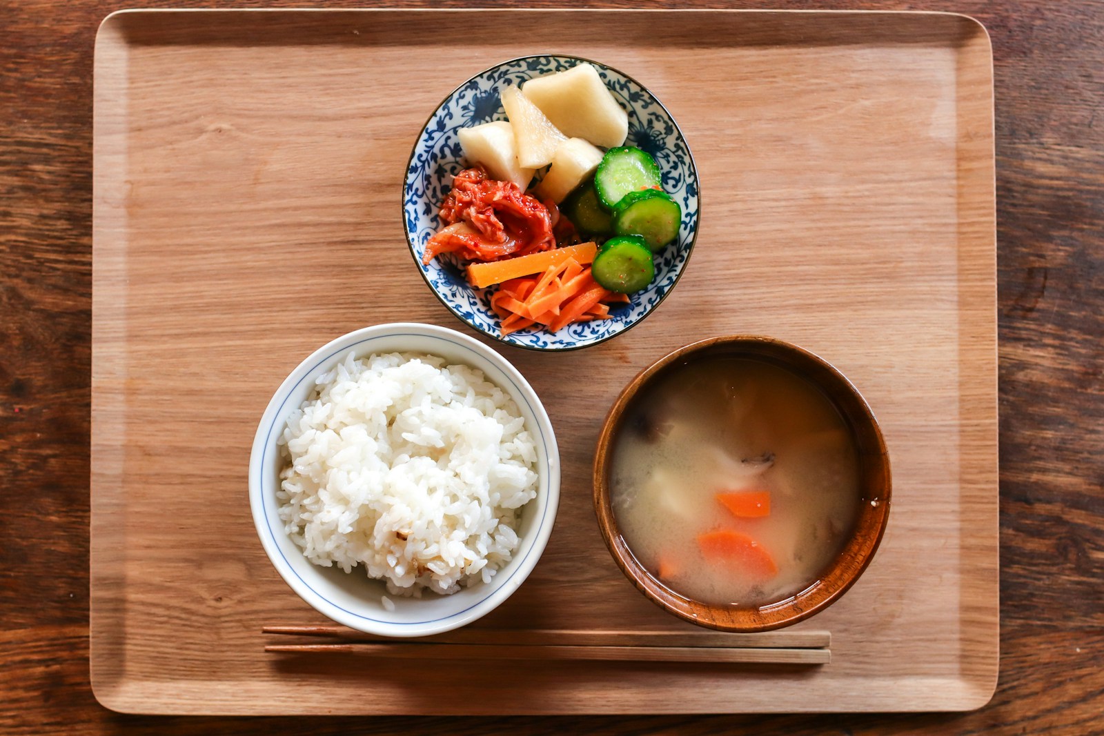 木のトレーにのった、白いご飯の茶碗と具だくさんの汁物の椀、漬物の小鉢と箸