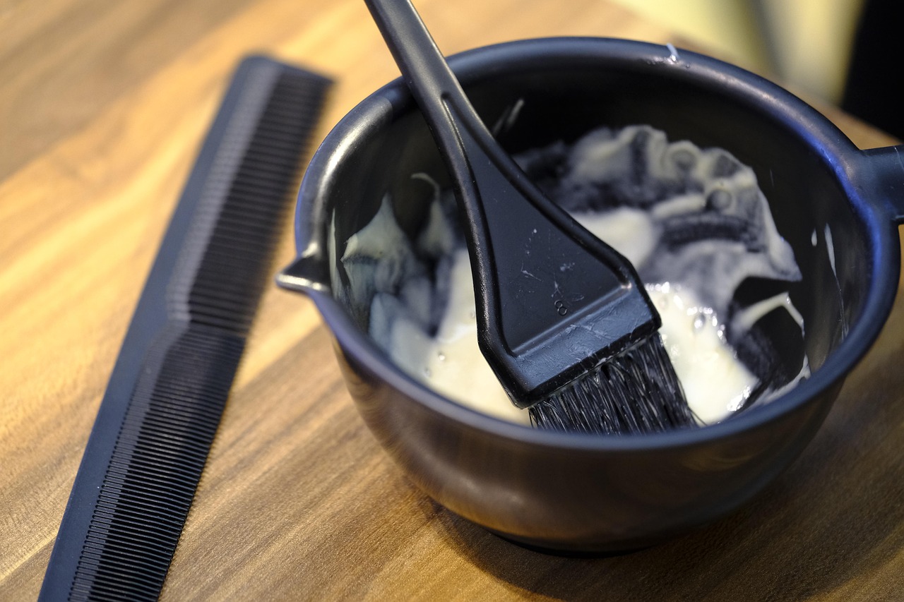 木目の台の上の黒いボウルに、白っぽい薬剤と黒いはけが入っている。左に黒いコームが置かれている