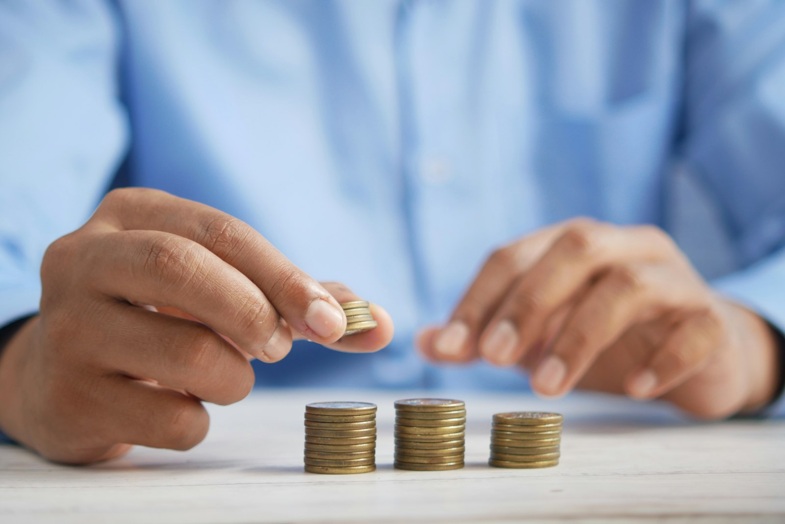 白い木の机の上に硬貨を3つの山に積み、右手で硬貨をつまんで山にのせようとしている手元