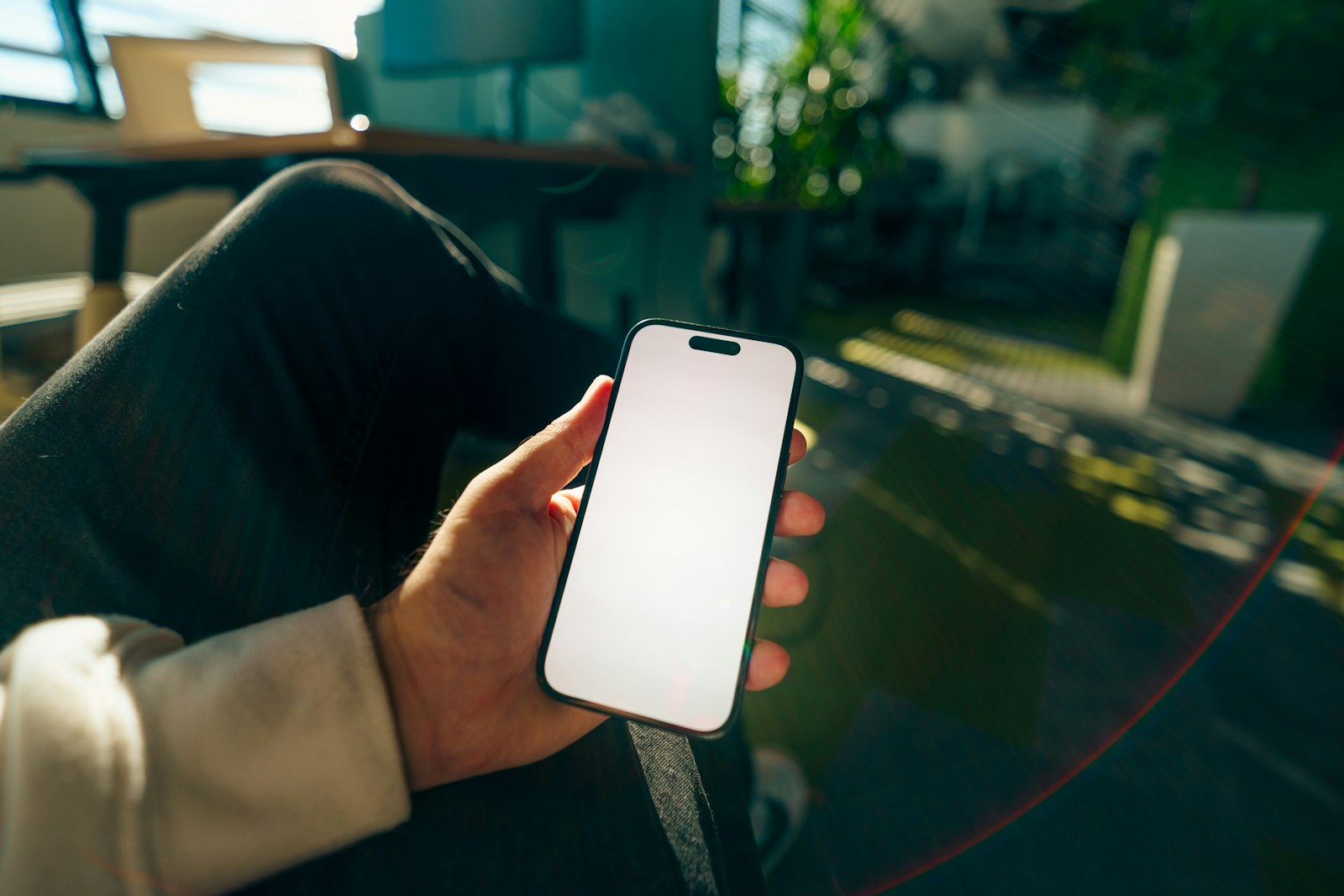 座った膝の上で片手にスマートフォンを持ち、何も表示されていない白い画面を見ている手元